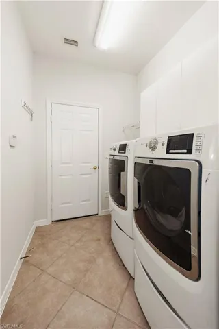 Laundry area featuring washing machine and dryer, light tile patterned floors, and cabinet space