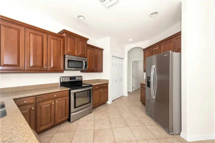Kitchen featuring appliances with stainless steel finishes, arched walkways, light tile patterned floors, recessed lighting, and light stone countertops
