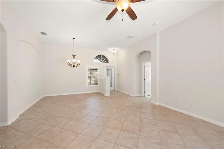 Unfurnished room featuring arched walkways, ceiling fan, light tile patterned floors, and a chandelier