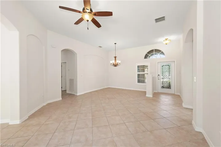 Empty room with arched walkways, light tile patterned floors, a ceiling fan, and a chandelier