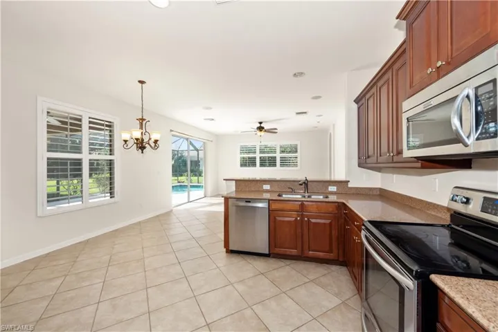 Kitchen with stainless steel appliances, a peninsula, pendant lighting, light tile patterned floors, and light stone countertops