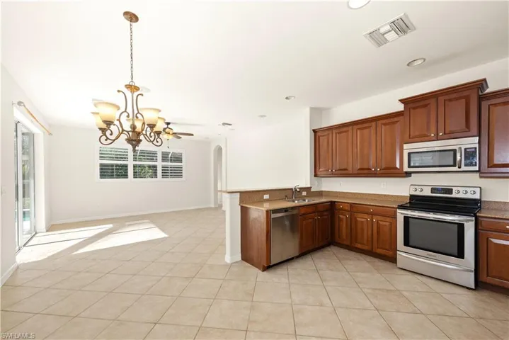 Kitchen featuring stainless steel appliances, open floor plan, pendant lighting, arched walkways, and a chandelier