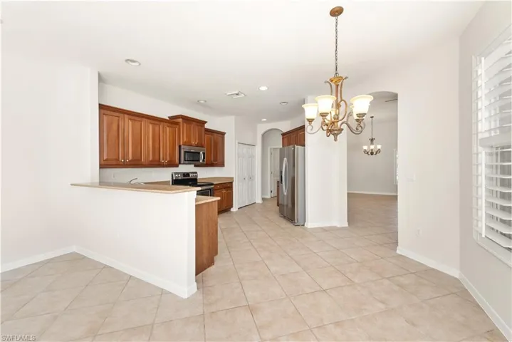 Kitchen with arched walkways, pendant lighting, appliances with stainless steel finishes, brown cabinets, and a peninsula