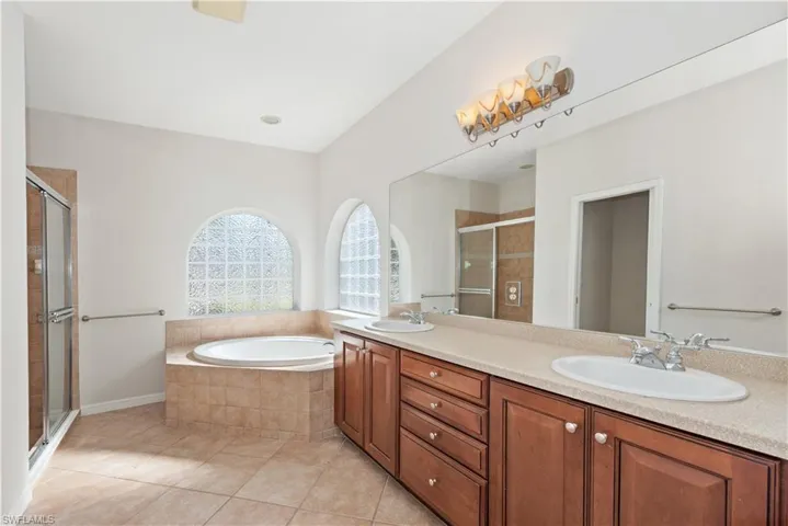 Full bath featuring double vanity, a stall shower, a garden tub, and light tile patterned flooring