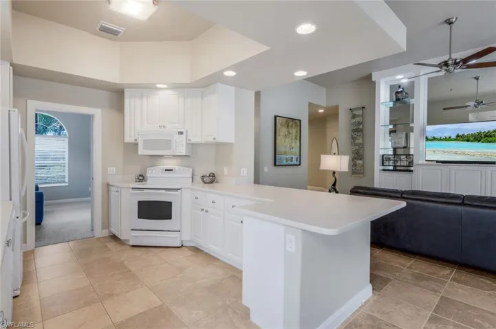 Kitchen featuring light colored carpet, white appliances, white cabinets, and kitchen peninsula