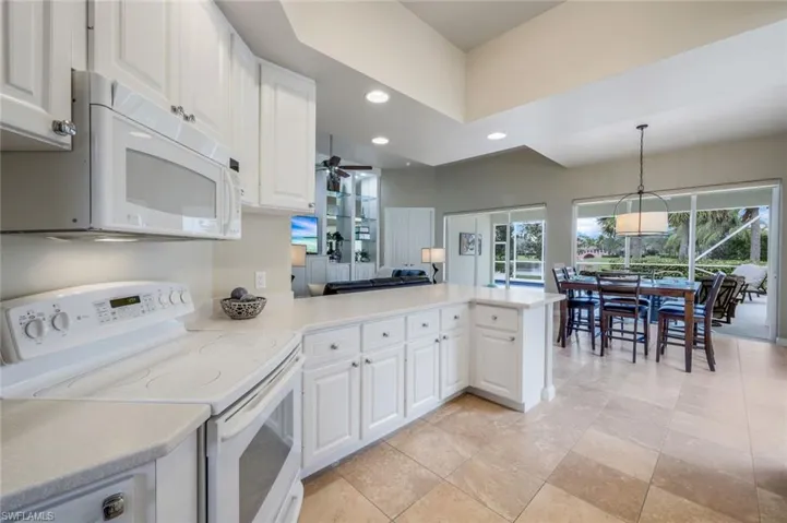 Kitchen with white appliances, white cabinets, kitchen peninsula, and hanging light fixtures