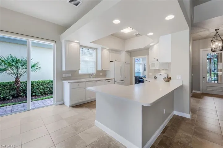 Kitchen featuring kitchen peninsula, sink, white appliances, white cabinets, and a chandelier