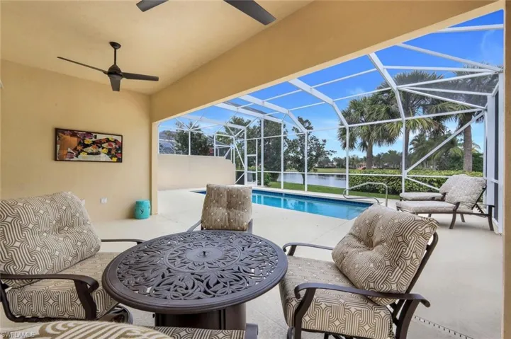 View of pool with ceiling fan, glass enclosure, a water view, and a patio