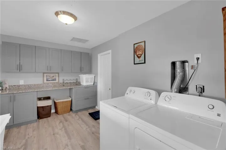 Washroom featuring light wood-type flooring, washing machine and dryer, and cabinet space
