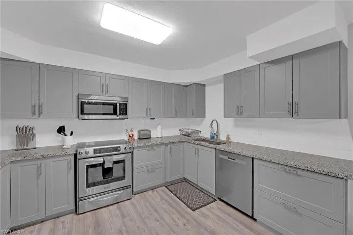 Kitchen featuring gray cabinetry, stainless steel appliances, light wood finished floors, and light stone counters