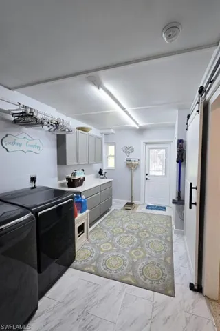 Clothes washing area with a barn door, washer and dryer, and light tile floors