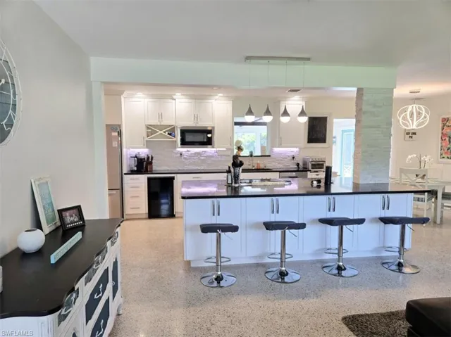 Kitchen featuring stainless steel appliances, beverage cooler, backsplash, and decorative light fixtures