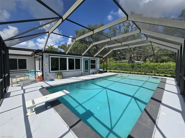 View of swimming pool featuring a patio, a diving board, and glass enclosure