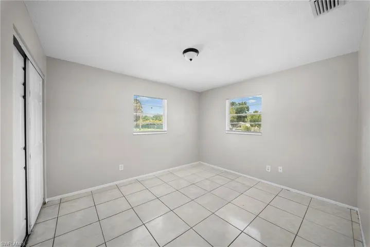 Unfurnished bedroom featuring a closet, multiple windows, light tile patterned floors, and a textured ceiling