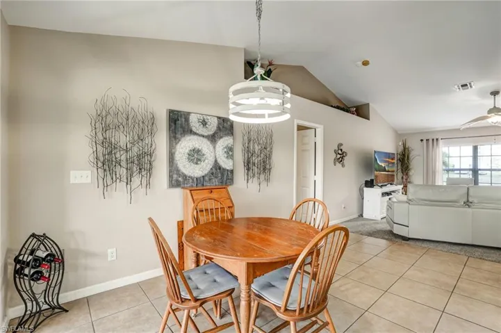 Dining area featuring vaulted ceiling, light tile patterned floors, baseboards, and a ceiling fan