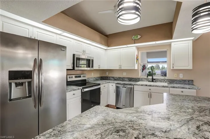 Kitchen featuring stainless steel appliances, a sink, white cabinets, a ceiling fan, and light stone countertops