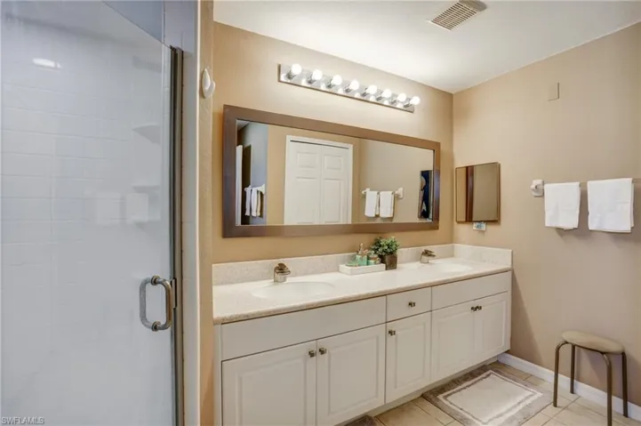 Full bathroom featuring double vanity, a shower stall, baseboards, and tile patterned flooring