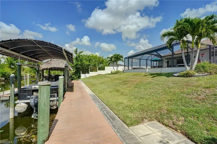View of yard with a boat dock, glass enclosure, a water view, and boat lift