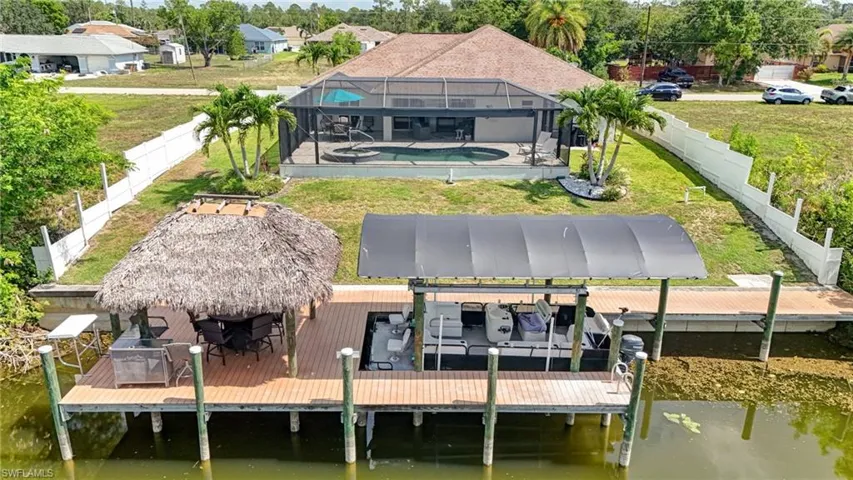 Rear view of house with boat lift, an outdoor pool, a water view, and a lanai