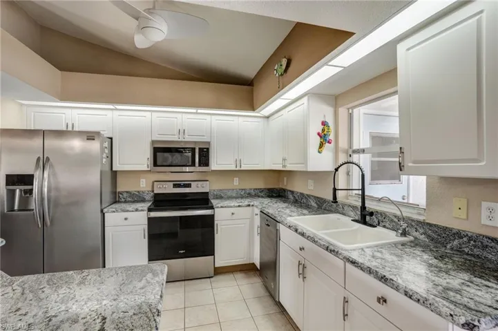 Kitchen with stainless steel appliances, a sink, ceiling fan, white cabinetry, and vaulted ceiling