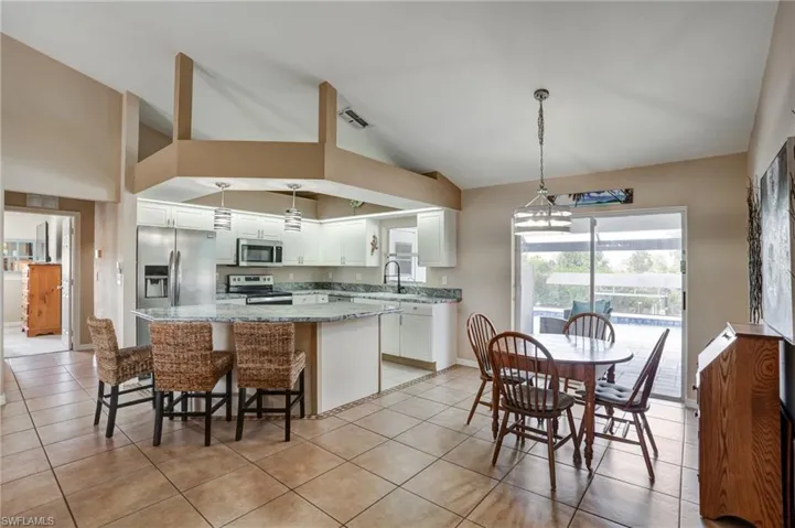 Kitchen featuring appliances with stainless steel finishes, light tile patterned floors, high vaulted ceiling, white cabinetry, and a center island
