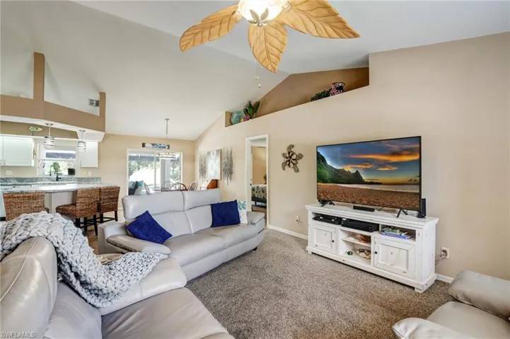 Living area with ceiling fan, light colored carpet, baseboards, and high vaulted ceiling