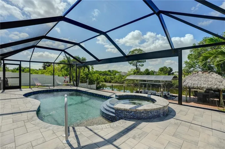 View of swimming pool featuring a pool with connected hot tub, a patio area, and glass enclosure