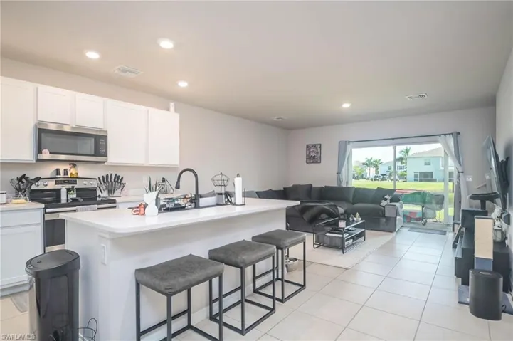 Kitchen featuring light tile patterned flooring, a kitchen bar, appliances with stainless steel finishes, a kitchen island with sink, and white cabinets