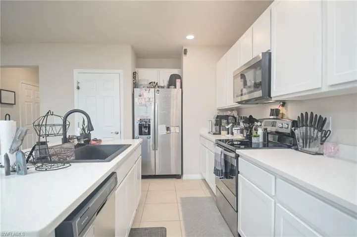 Kitchen featuring appliances with stainless steel finishes, sink, light tile patterned floors, and white cabinets