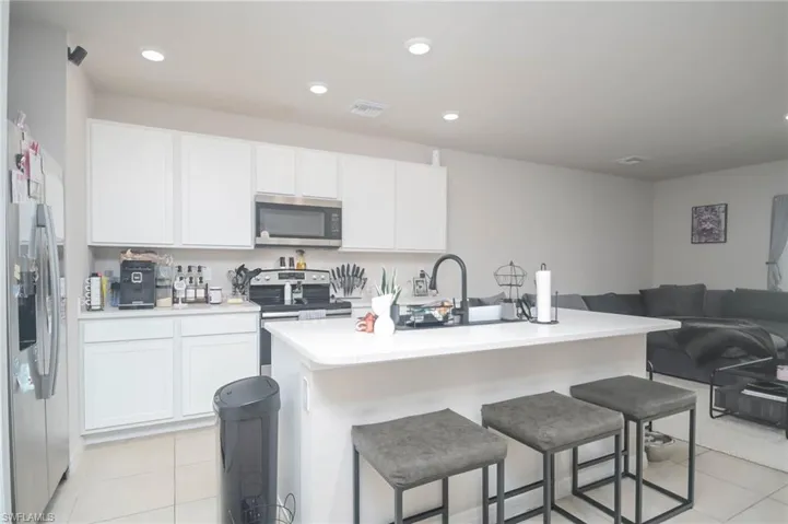 Kitchen with a kitchen island with sink, light tile patterned floors, stainless steel appliances, and white cabinets