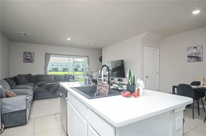 Kitchen featuring white cabinetry, light tile patterned floors, stainless steel dishwasher, and a center island with sink