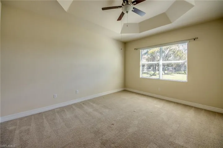 Empty room with light carpet, baseboards, a tray ceiling, and ceiling fan