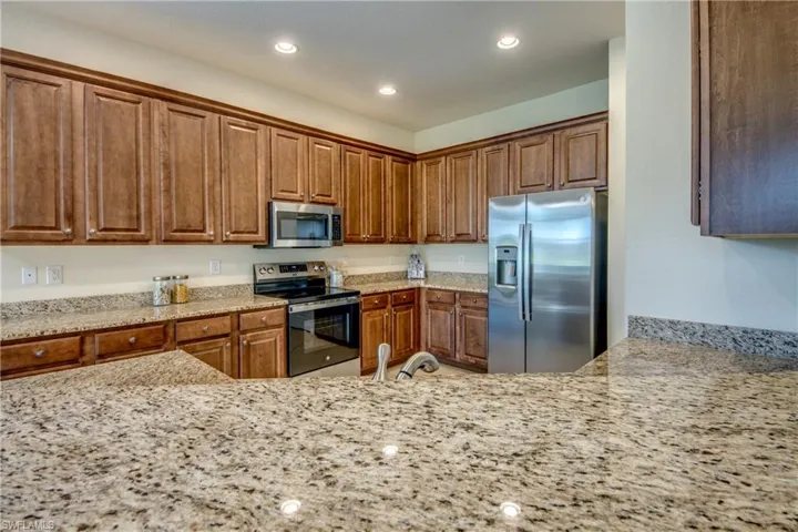 Kitchen with light stone counters, recessed lighting, brown cabinets, and appliances with stainless steel finishes