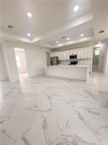 Unfurnished living room featuring a tray ceiling, recessed lighting, baseboards, and a sink