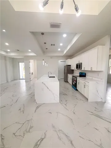 Kitchen featuring stainless steel appliances, a sink, a tray ceiling, white cabinetry, and open floor plan