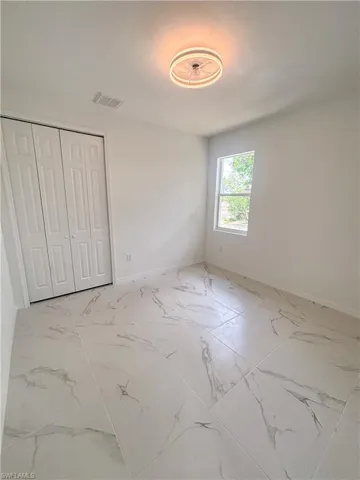 Unfurnished bedroom featuring light marble finish floors, baseboards, and a closet