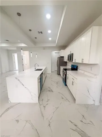 Kitchen with appliances with stainless steel finishes, a sink, light marble finish floors, white cabinets, and light stone countertops