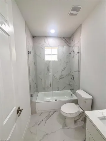 Full bathroom with enclosed tub / shower combo, vanity, toilet, baseboards, and marble finish flooring