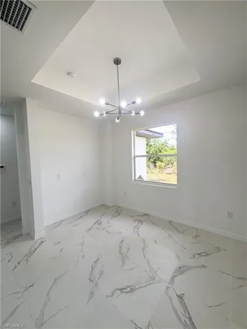Unfurnished room featuring a tray ceiling, baseboards, and a chandelier