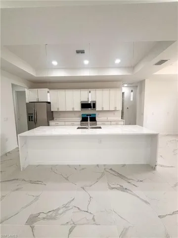 Kitchen with appliances with stainless steel finishes, a tray ceiling, a sink, white cabinets, and recessed lighting