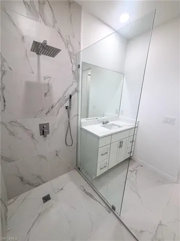 Full bathroom with marble finish floors, a marble finish shower, vanity, and baseboards