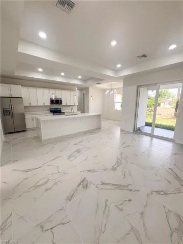 Unfurnished living room with a tray ceiling, a chandelier, a sink, recessed lighting, and baseboards