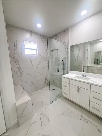 Bathroom with a marble finish shower, vanity, marble finish floors, and recessed lighting