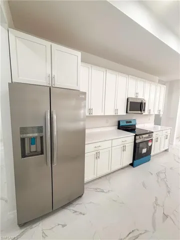 Kitchen featuring appliances with stainless steel finishes, light marble finish floors, white cabinets, and light countertops