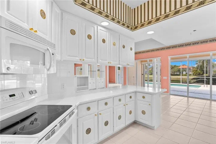 Kitchen with white appliances, white cabinetry, light tile patterned floors, a peninsula, and backsplash