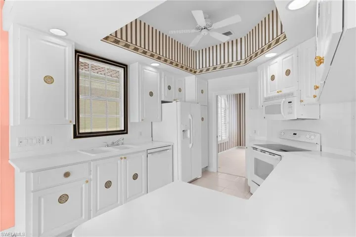 Kitchen with white appliances, light countertops, plenty of natural light, and white cabinetry