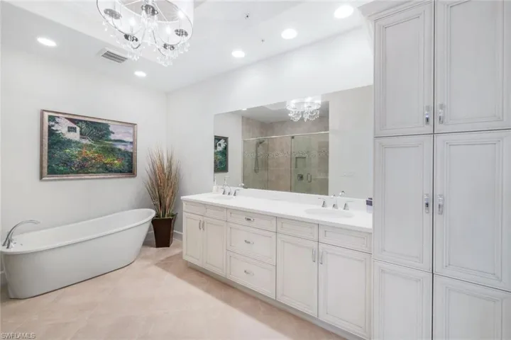 Bathroom with a chandelier, a stall shower, double vanity, a soaking tub, and recessed lighting