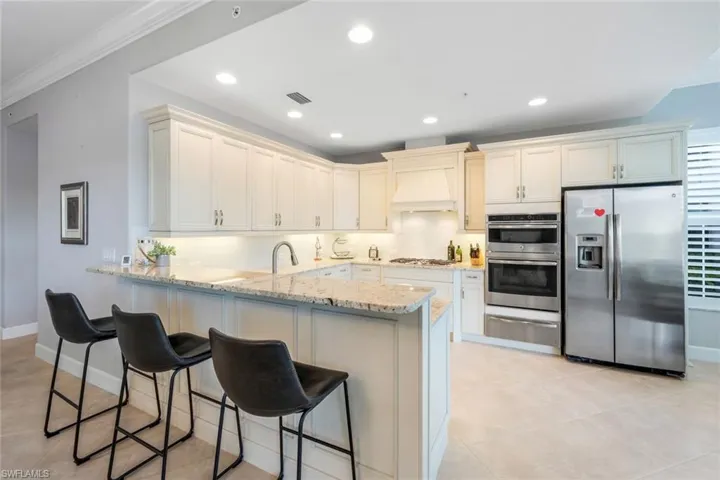 Kitchen with stainless steel appliances, a peninsula, tasteful backsplash, light stone counters, and crown molding