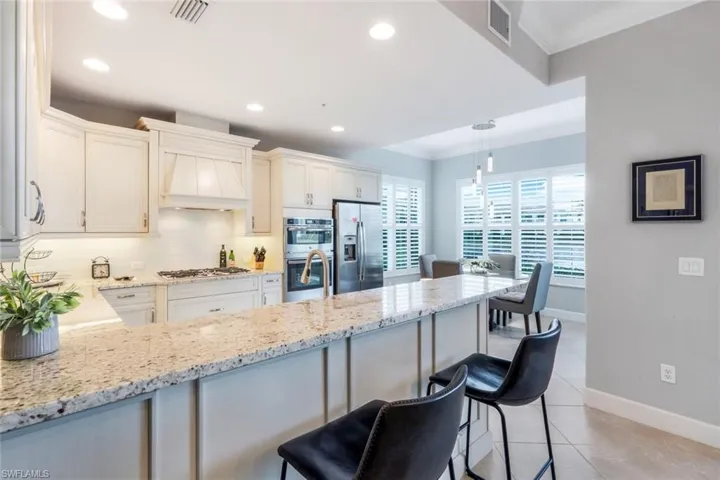 Kitchen with crown molding, decorative backsplash, a kitchen bar, appliances with stainless steel finishes, and light stone countertops