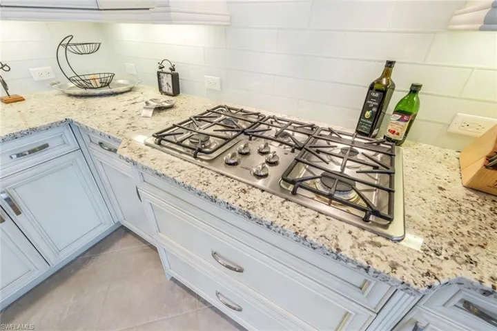 Kitchen with stainless steel gas stovetop, light stone counters, decorative backsplash, and light tile patterned flooring